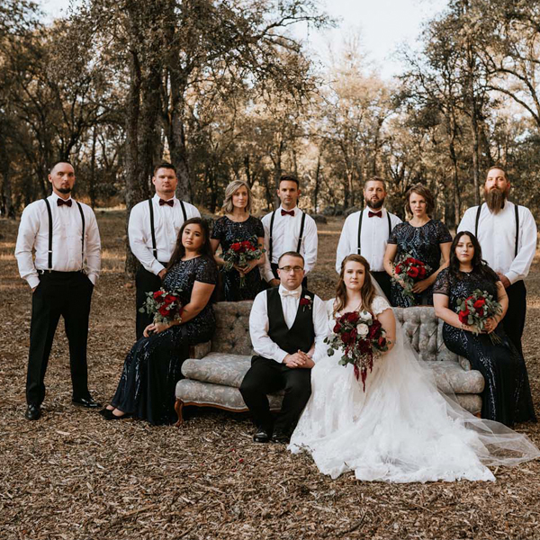 bride and groom sitting on a couch in the woods with their bridal party