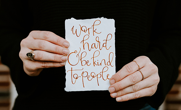 woman holding a piece of paper that says "Work hard and be kind to people"
